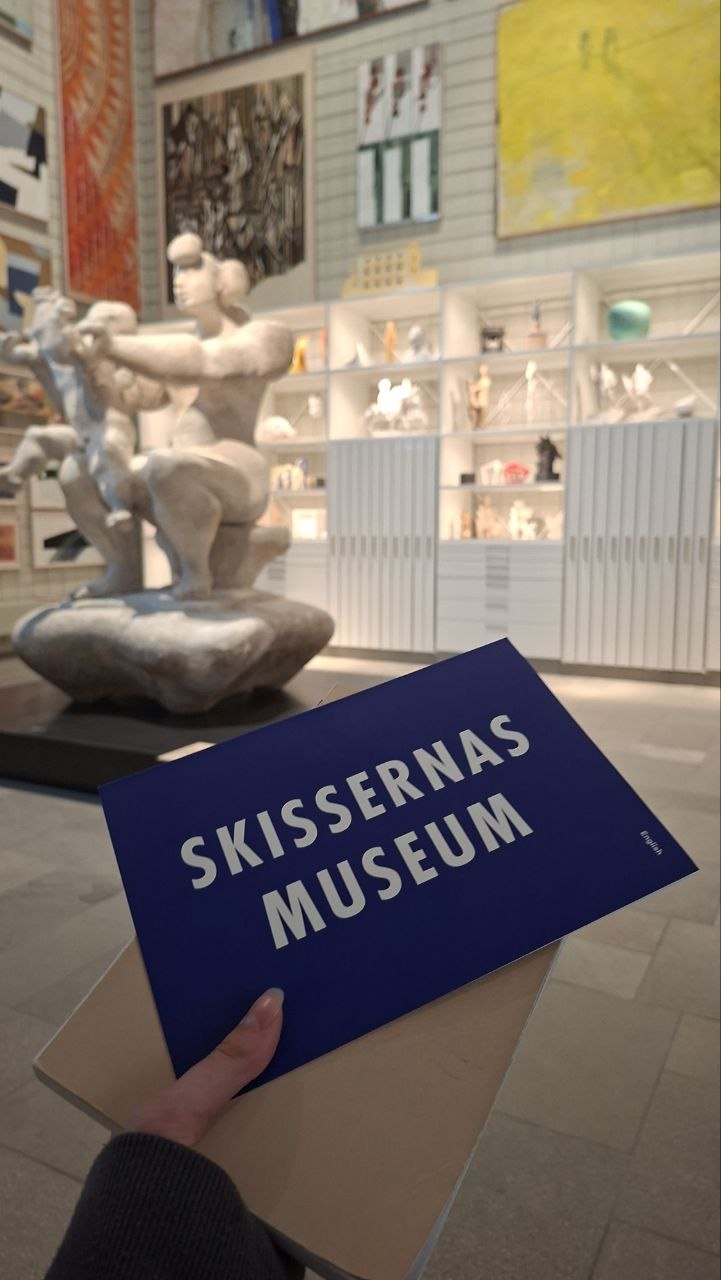 Брошура Skissernas Museum у руках відвідувачки, на тлі — експозиція музею